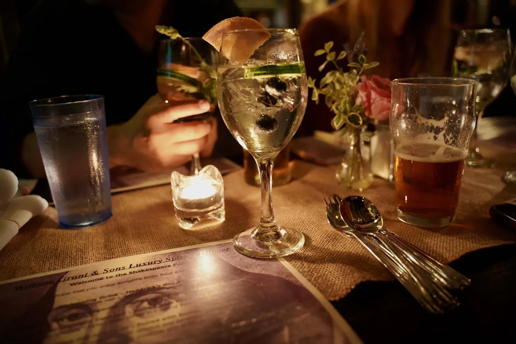 Dimly lit table with drinks, cutlery, candle, flowers, and a menu.