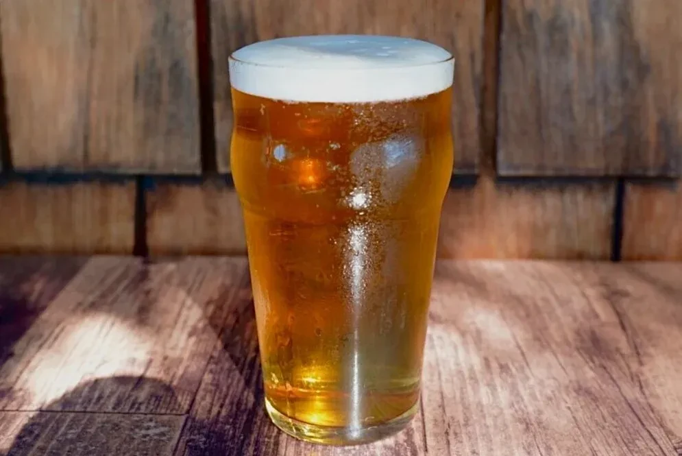 Chilled golden beer with foam in a pint glass on rustic wood.