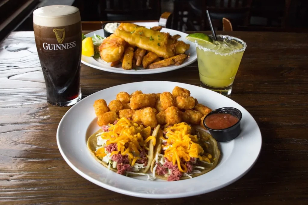 Tacos, tater tots, Guinness, fish and chips, margarita on pub table.