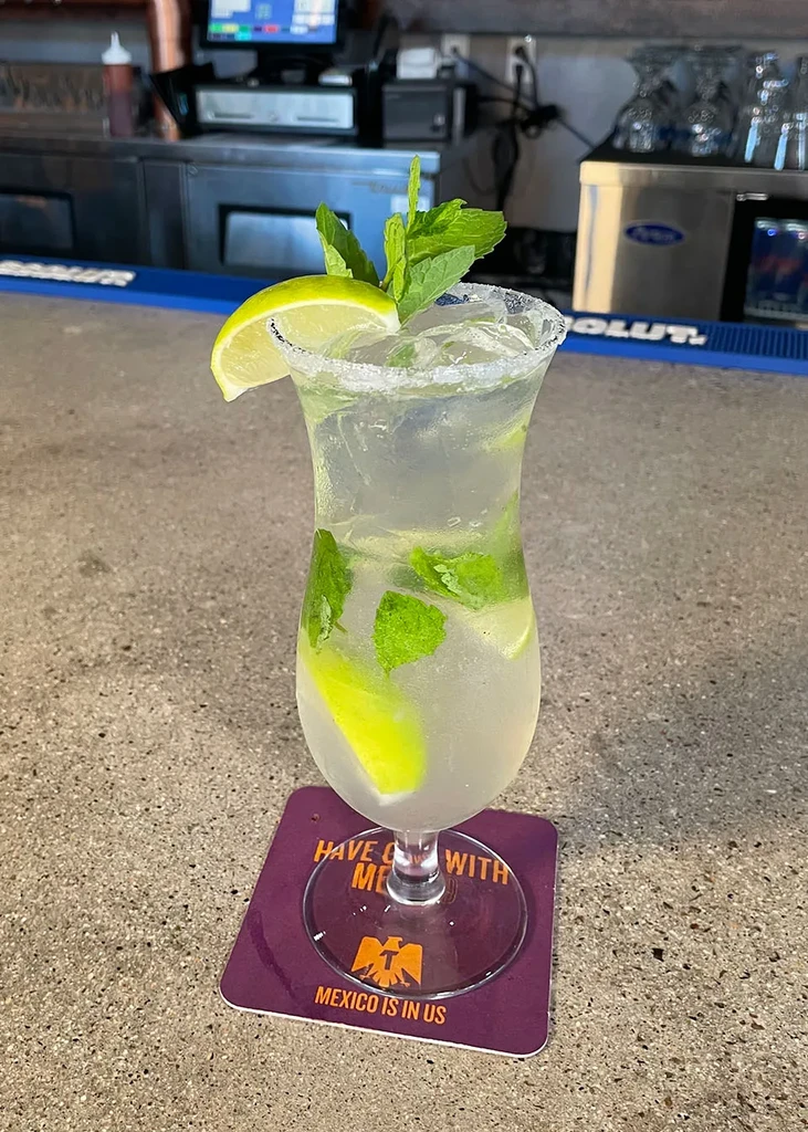 Clear cocktail with mint, lime, and salted rim in a hurricane glass.