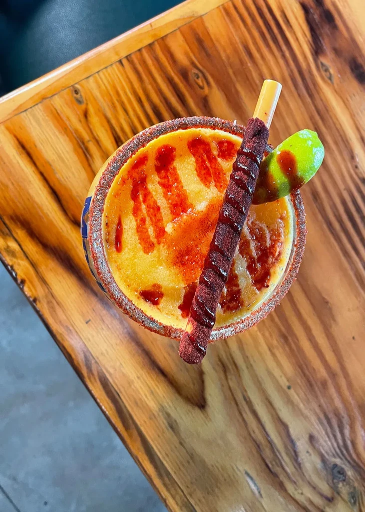 Spiced yellow-orange slushy drink with chili rim, lime, tamarind stick.