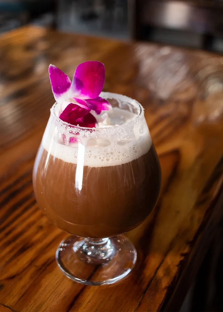 Multi-layered drink in stemmed glass with orchid and crystalline rim.