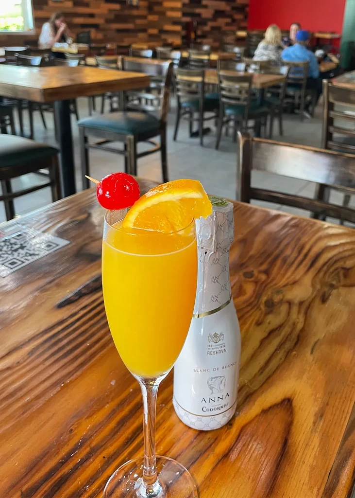 Mimosa with orange and cherry, sparkling wine, on a rustic table.