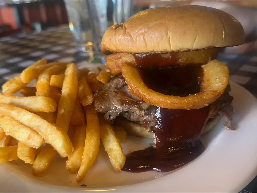 Brioche burger with pulled meat, onion rings, dripping BBQ sauce, and fries.