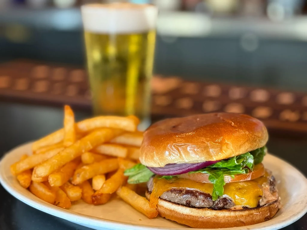 Gourmet cheeseburger, french fries, and a blurred glass of beer.