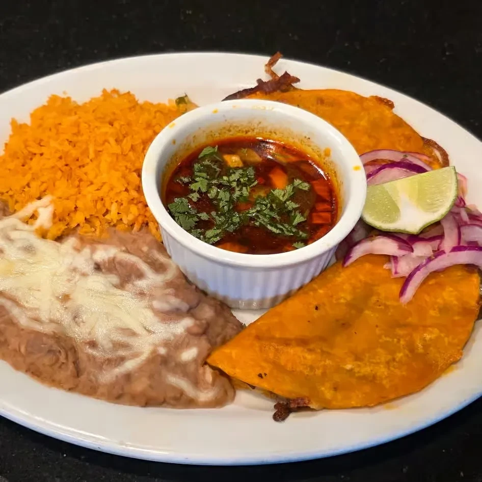 Mexican food plate with birria tacos, rice, beans, and cilantro consommé.
