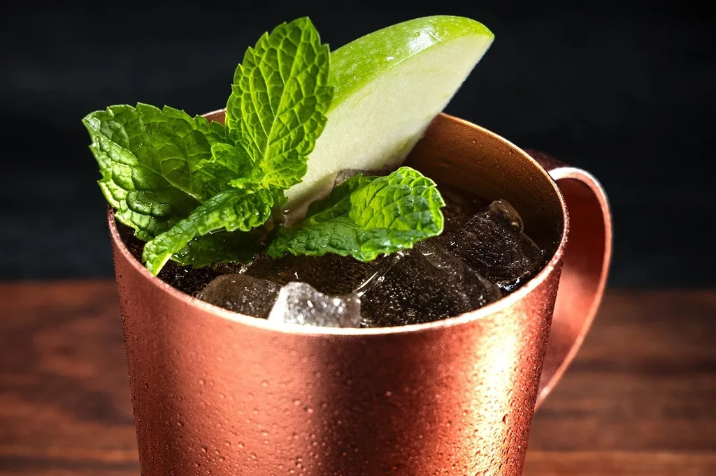 Cold Moscow Mule cocktail in a copper mug with mint and apple.