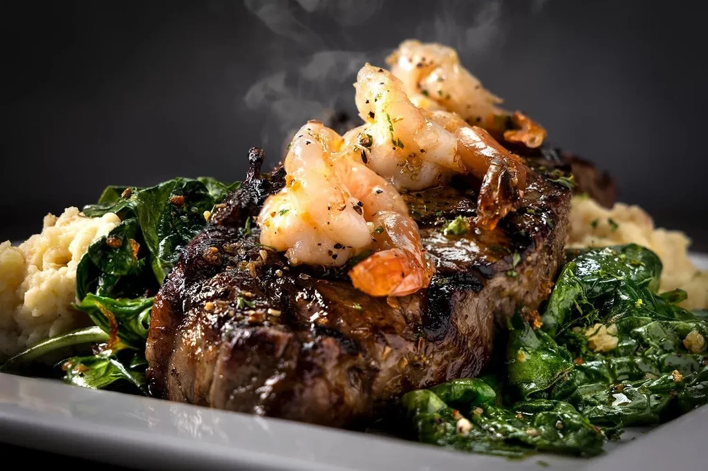 Steaming steak and grilled shrimp with mashed potatoes and green vegetables.