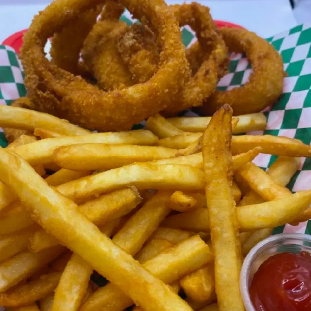 Crispy french fries and onion rings in a red basket with ketchup.