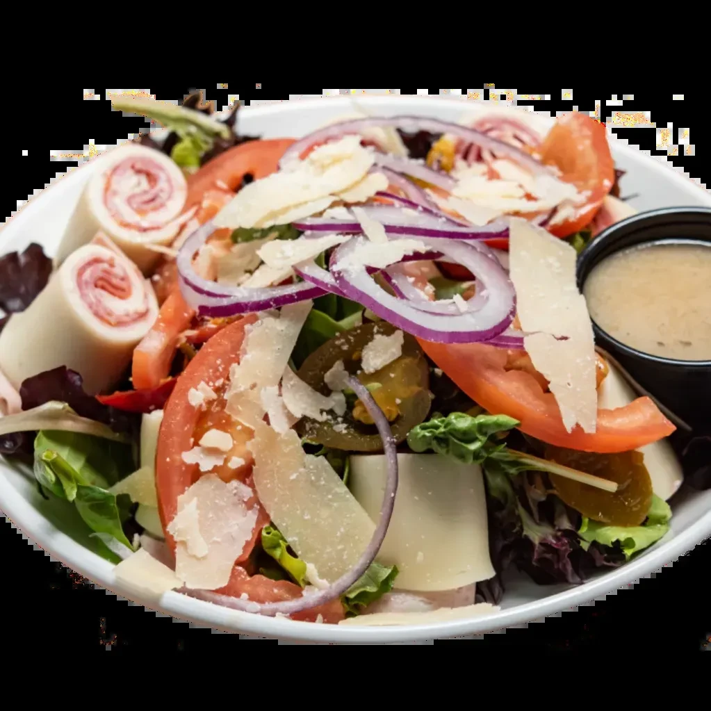 Fresh salad in white bowl with greens, deli meat, cheese, dressing.