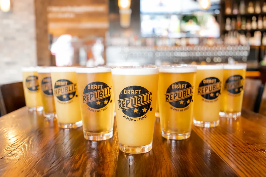 Pint glasses of light beer with "DRAFT REPUBLIC" logos on a table.
