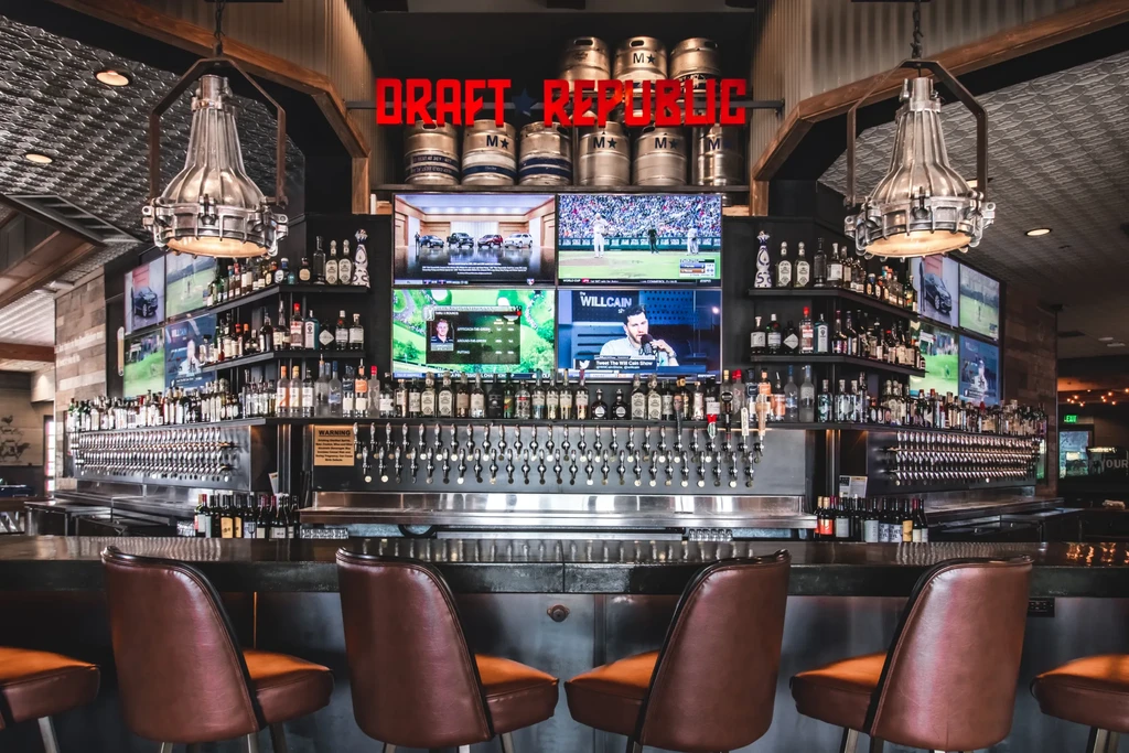 Industrial DRAFT REPUBLIC bar with taps, spirits, and multiple sports TVs.