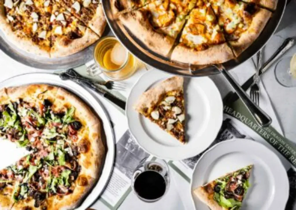 Overhead shot: three pizzas, drinks, and silverware on a themed table.