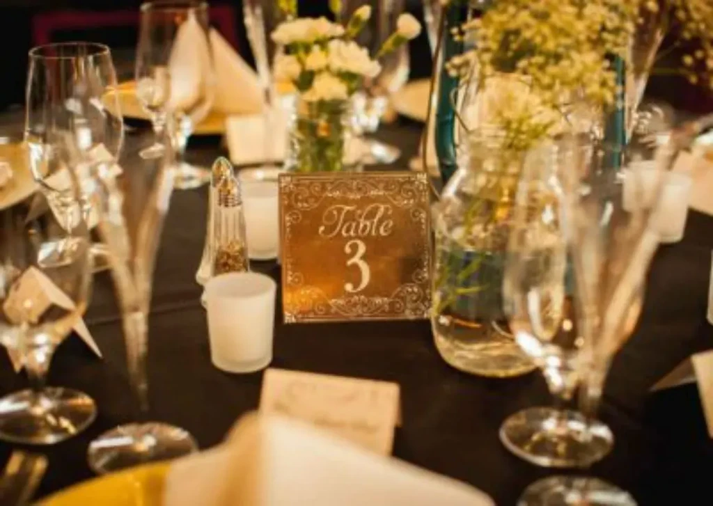 Elegant table setting with a gold "Table 3" sign, glasses, and flowers.