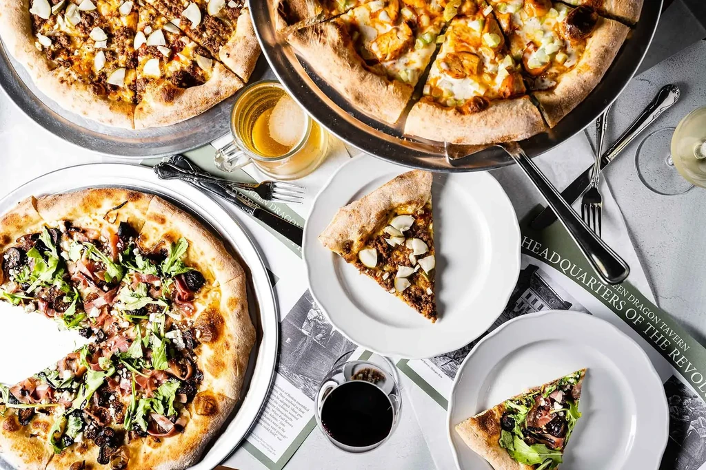 Overhead view of three pizzas, drinks, and Green Dragon Tavern placemat.