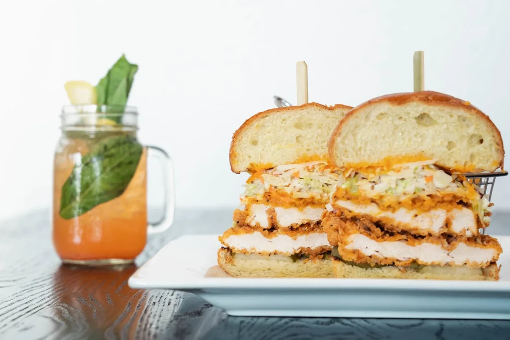 Fried chicken sandwich halves with coleslaw and a basil-garnished drink.