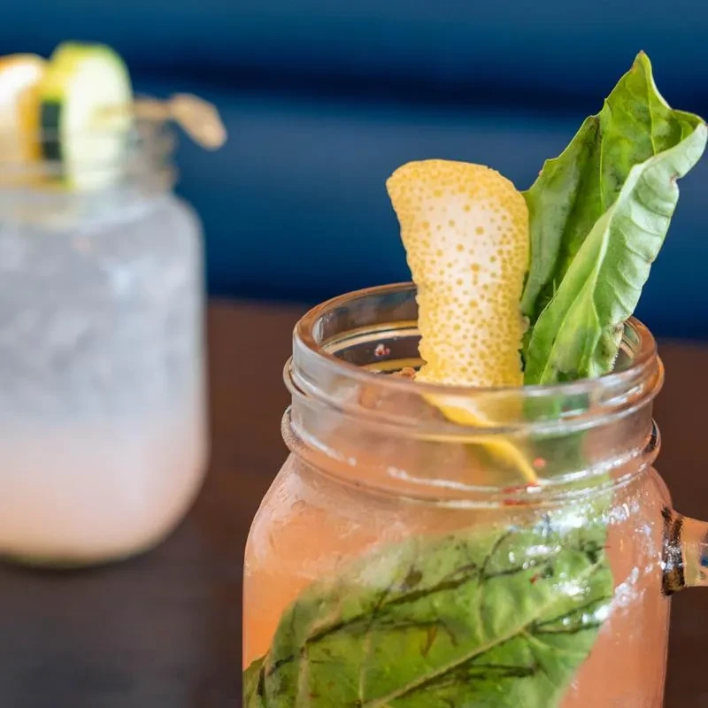 Reddish-orange drink with lemon peel and green leaves in a mason jar.