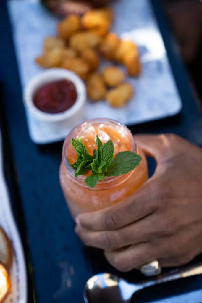 Close-up: Hand holds orange drink in jar with mint sprigs.