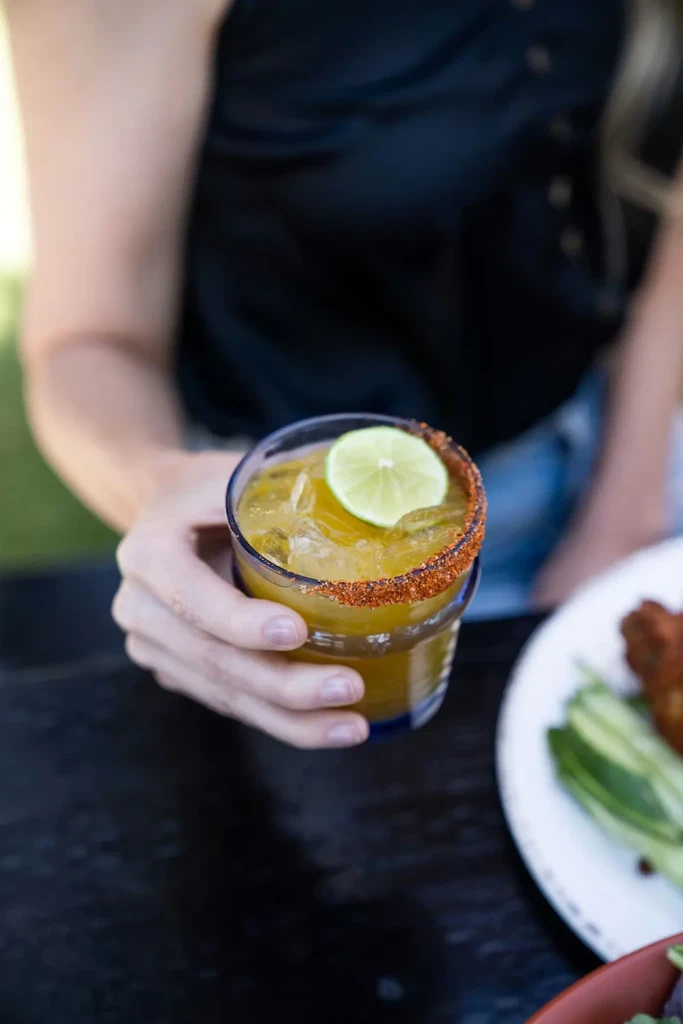 Hand holding a yellow-orange cocktail with a spiced rim and lime.