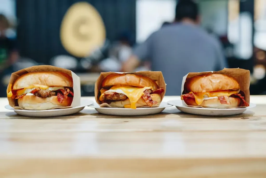 Three breakfast sandwiches with egg, bacon, sausage, and cheese.