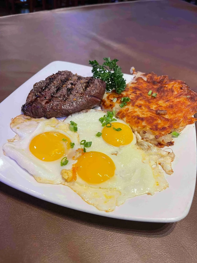 Plate of grilled steak, three fried eggs, and crispy hash browns.