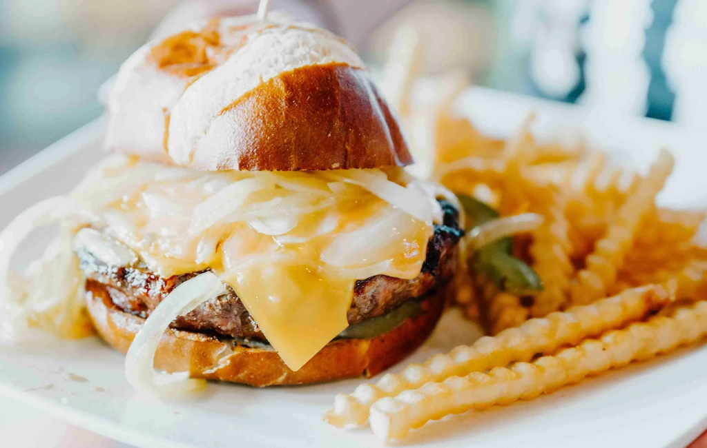 Grilled burger on pretzel bun with cheese, onions, and waffle fries.
