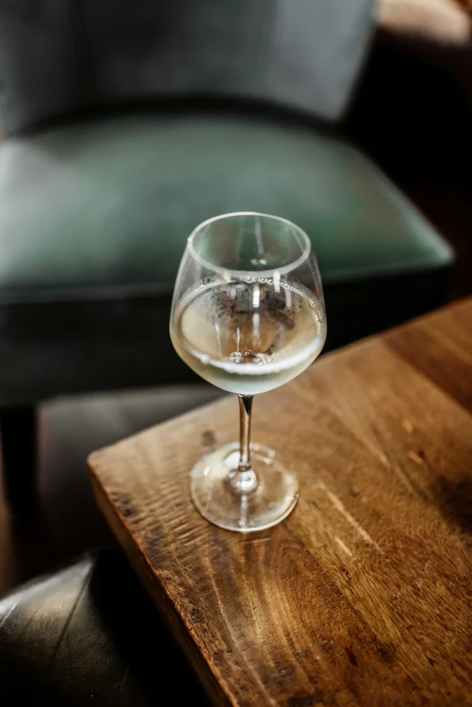 Frothy light beverage in wine glass on rustic dark wood table.