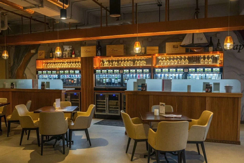 Upscale wine bar with modern dispensers, hanging glasses, and empty tables.