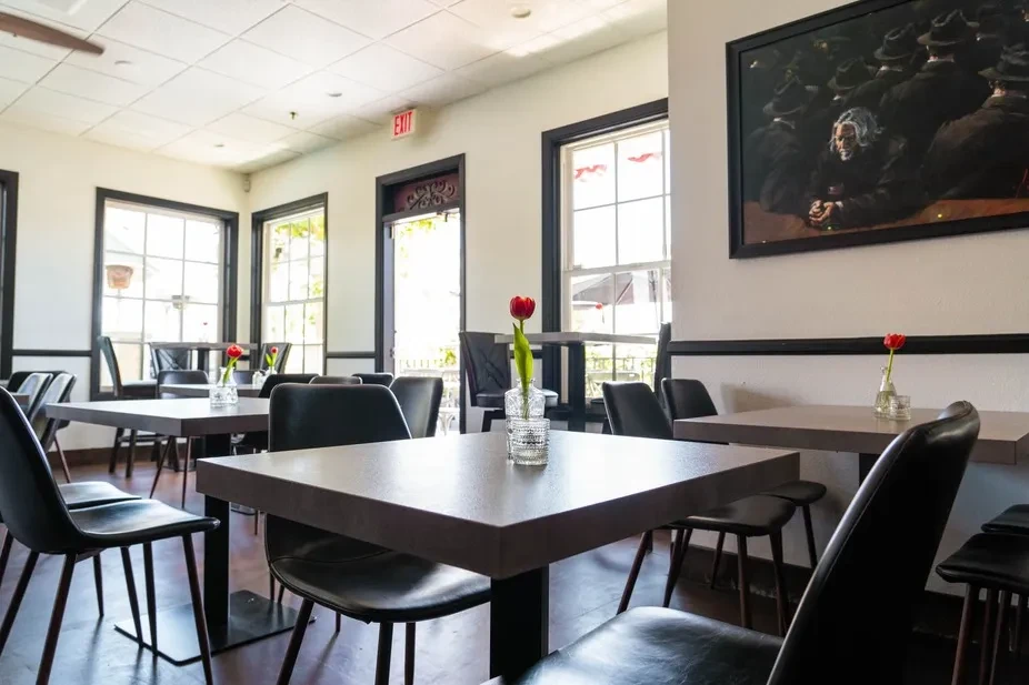 Well-lit empty dining room with tables, tulips, and a large painting.