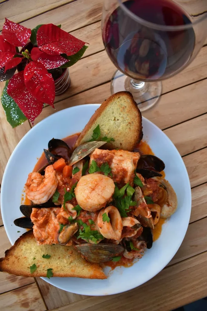 A vibrant seafood stew with bread, red wine, and festive plant.
