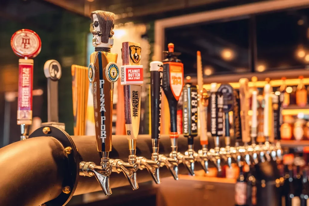 Colorful beer tap handles for various breweries in a bar.