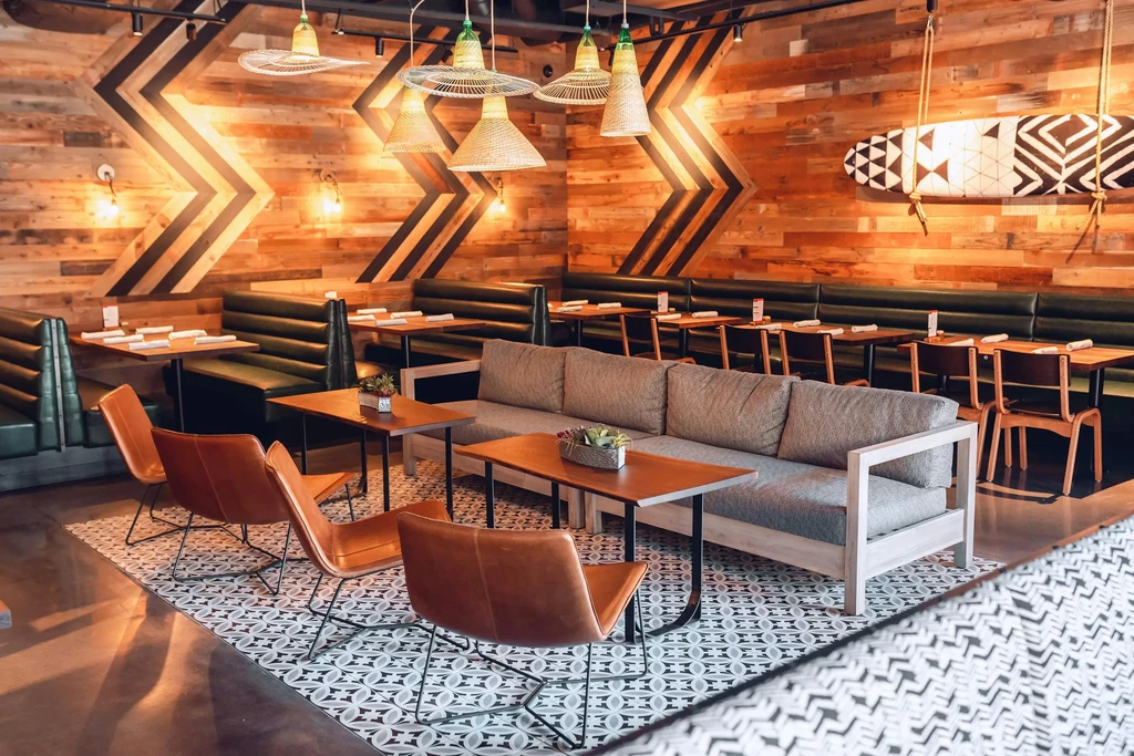 Restaurant interior with wood walls, varied seating, rattan lights, and tribal surfboard.