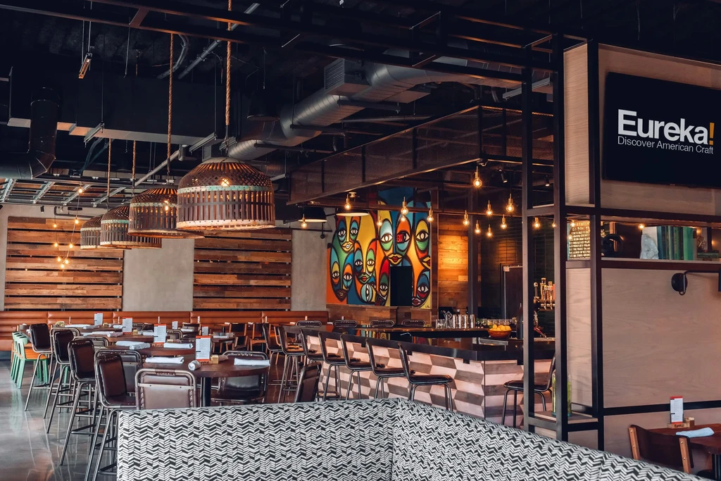 Empty industrial-chic restaurant interior featuring bar, dining, and vibrant mural.