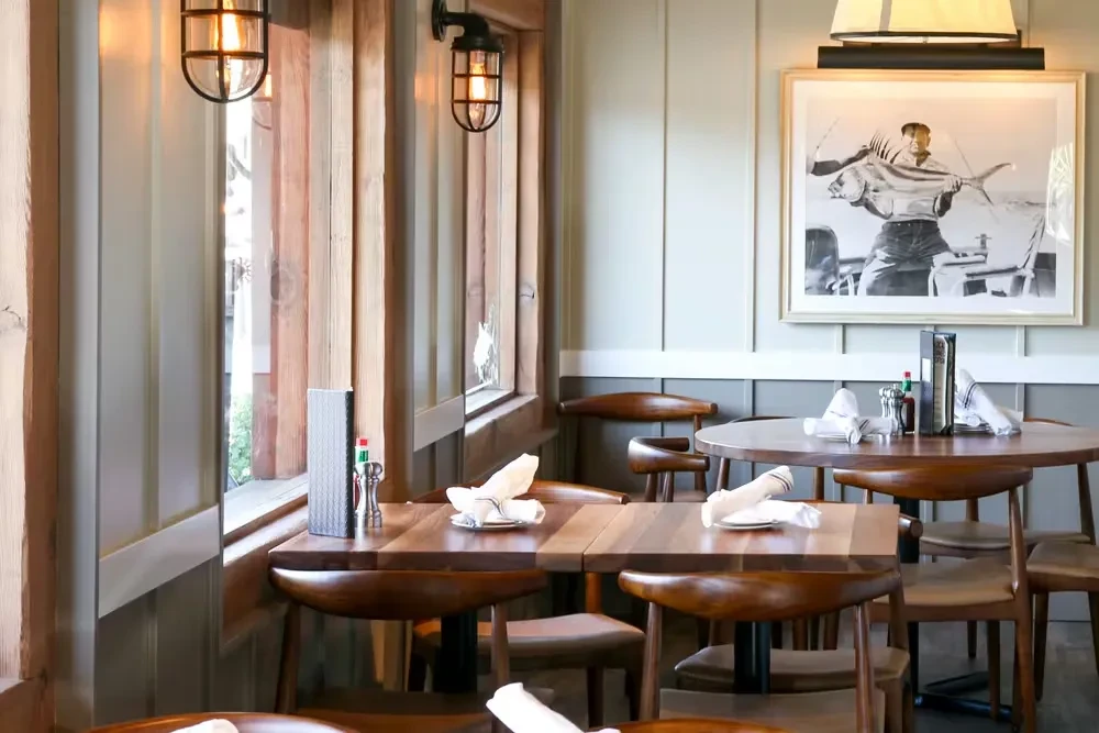 Empty restaurant dining room with wooden tables, chairs, and framed fish picture.