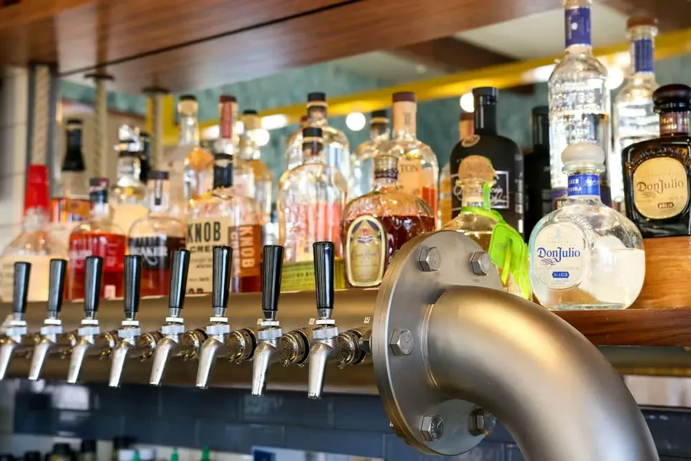 Ten silver beer taps below a shelf of spirit bottles.