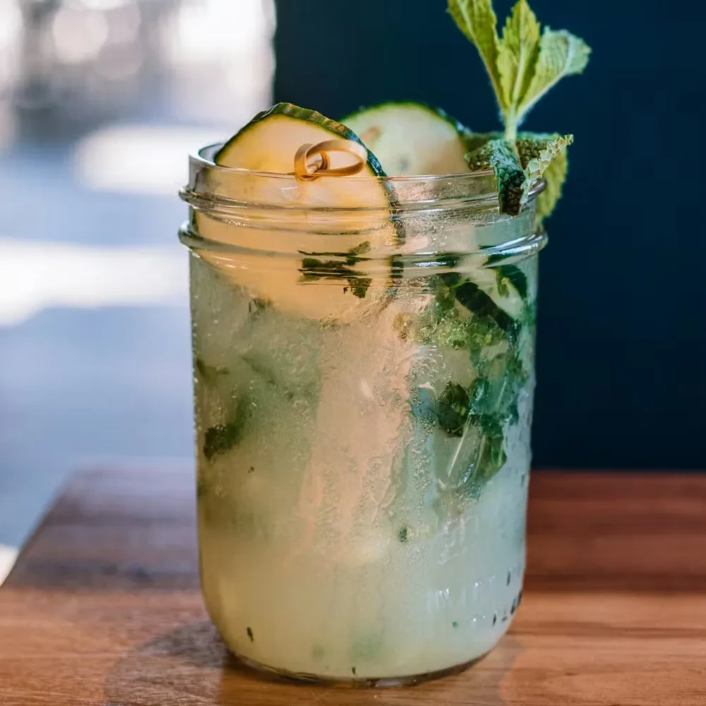 Mason jar with cold green drink, mint, cucumber, on wood.