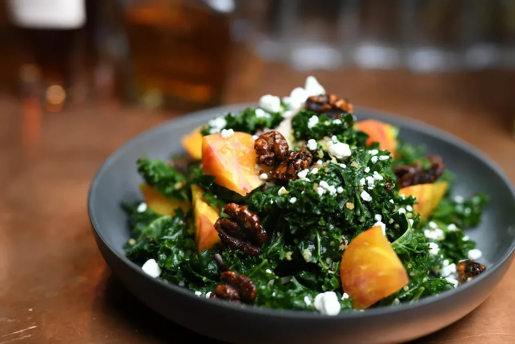 Close-up of vibrant kale salad with fruit, crumbled cheese, and nuts.