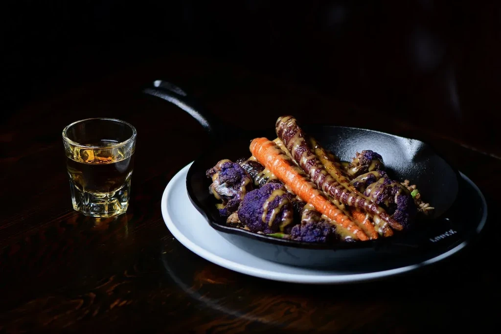 Roasted purple cauliflower and carrots in a skillet with a spirit shot.