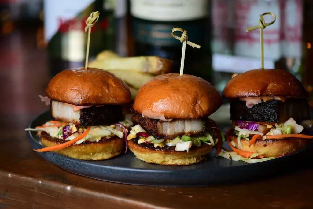 Three pork belly sliders with coleslaw and brioche buns.