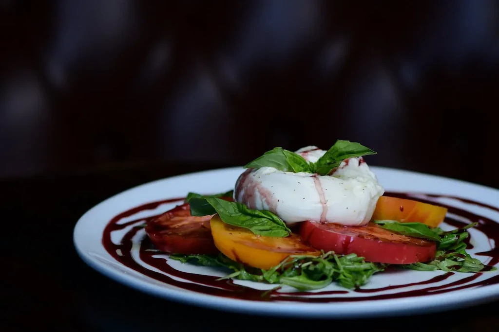 Creamy burrata, colorful heirloom tomatoes, basil, and dark sauce on a plate.