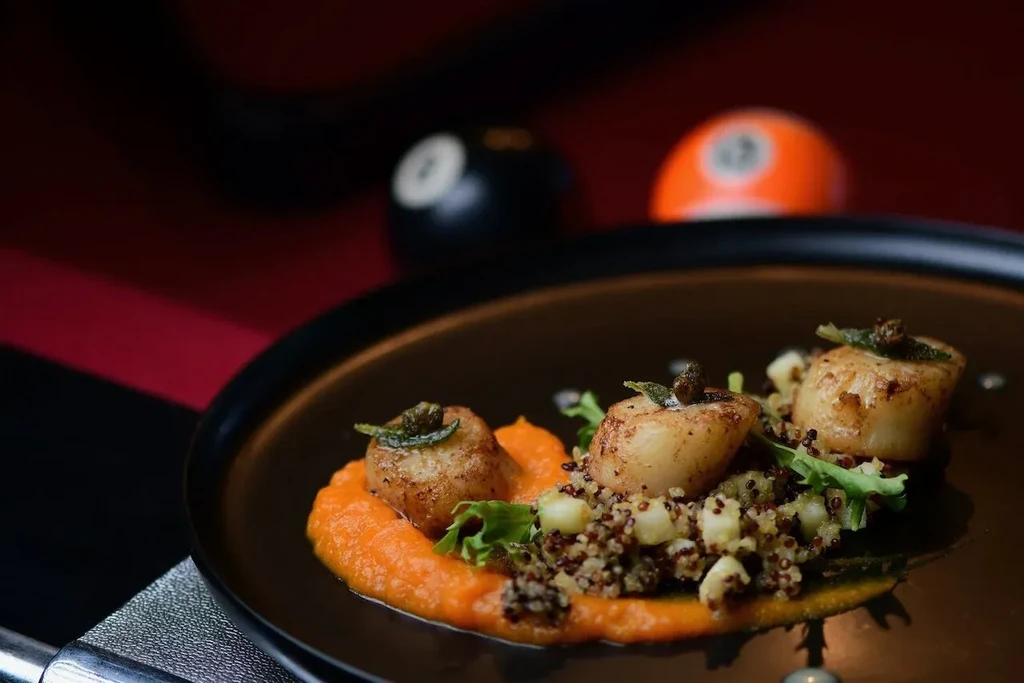 Three pan-seared scallops, orange puree, quinoa, and blurred billiard balls.