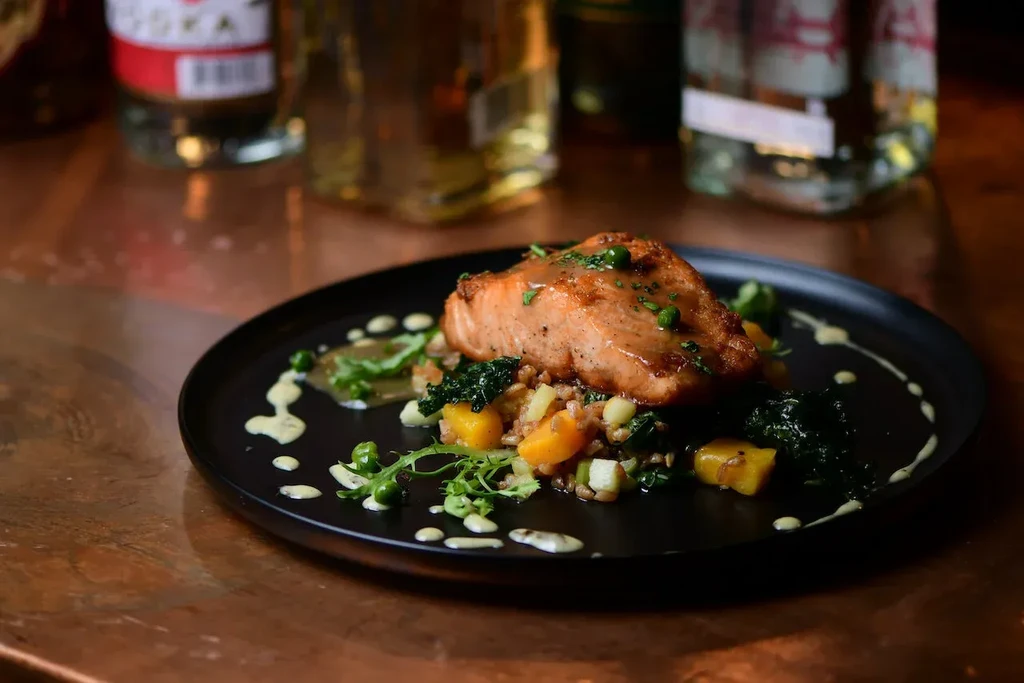 Seared salmon with peas, grains, vegetables, and sauce on a black plate.