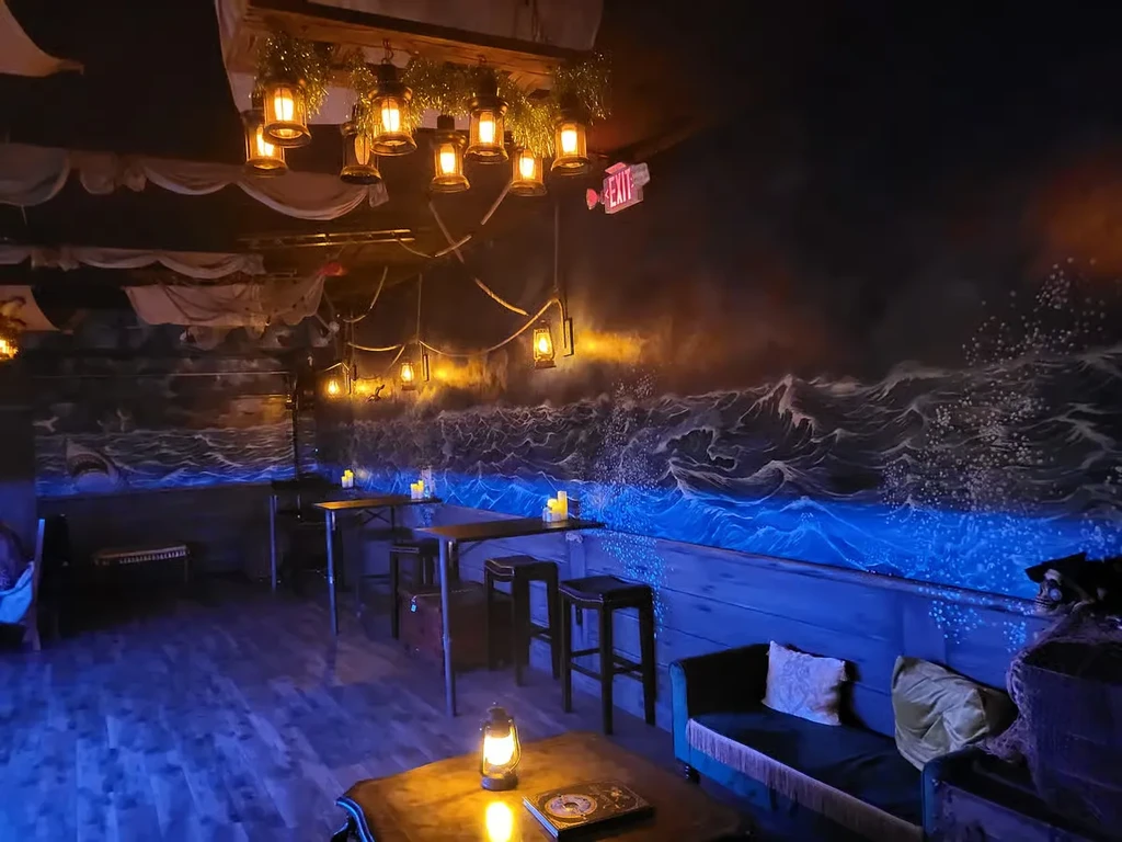 Dark nautical restaurant interior with warm lanterns, blue wave mural, and sails.