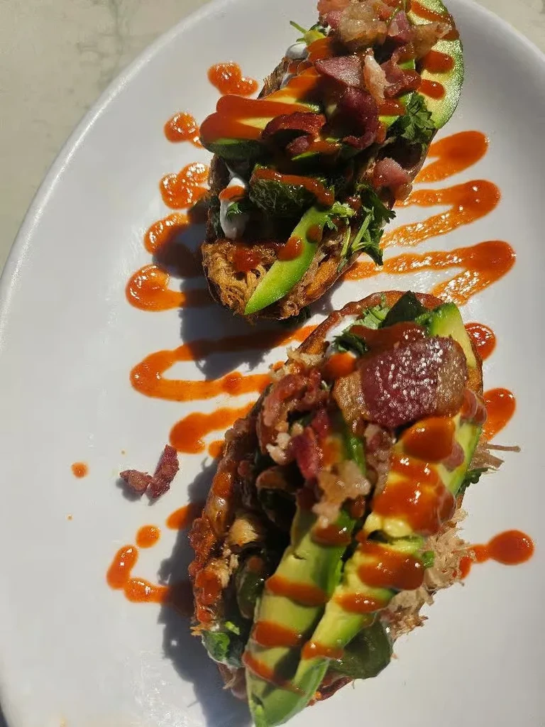 Elaborate loaded dishes with avocado, bacon, herbs, and two sauces.