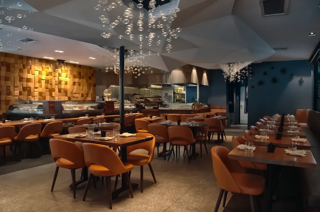 Upscale restaurant interior, burnt orange chairs, open kitchen, sphere chandeliers.