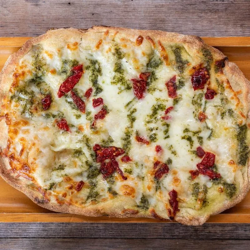 Oval flatbread pizza with melted cheese, pesto, and tomatoes.