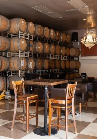 Warm wine bar with stacked barrels, seating, and elegant chandelier.