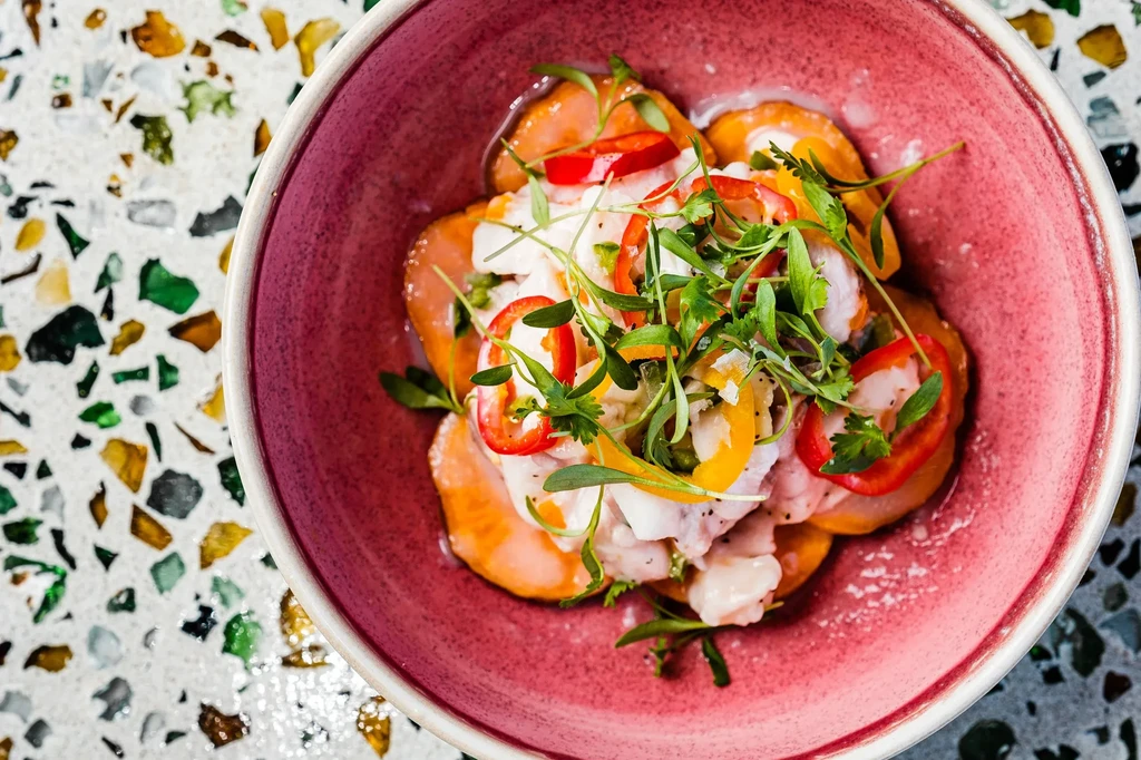 Vibrant seafood and vegetable dish in pink bowl on terrazzo.