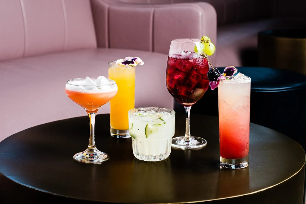 Five colorful, garnished cocktails on a table in an upscale lounge.