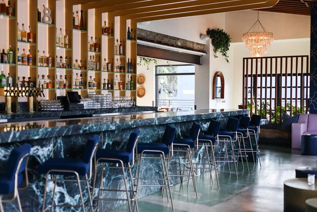 Empty modern bar with dark green marble counter and blue velvet stools.